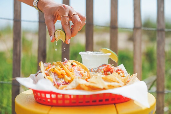 Une main saupoudrant des épices sur une assiette de nachos, avec une boisson à côté.