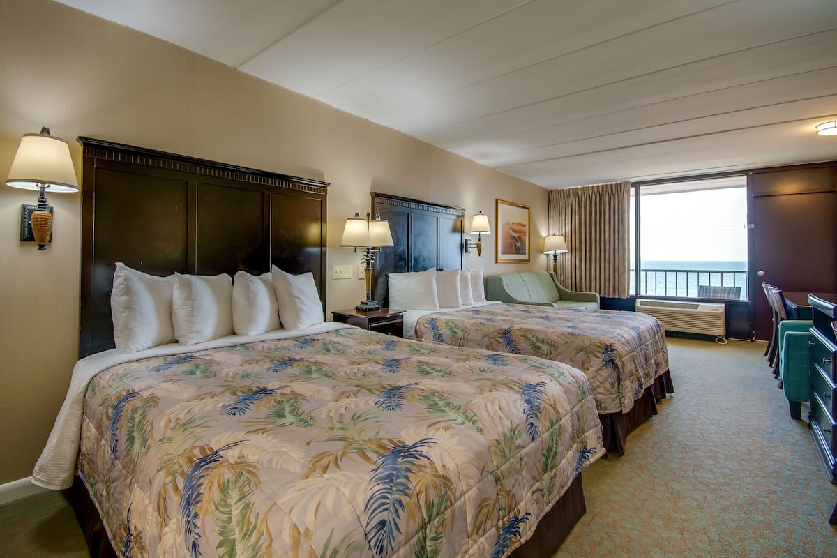 A hotel room with two beds, a desk, a chair, and a large window with curtains.