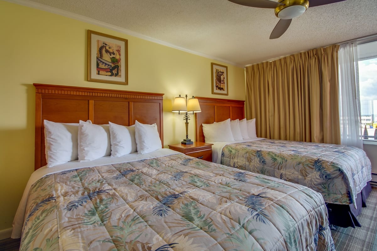 A hotel room with two beds, a wooden headboard, a ceiling fan, and a large window with curtains.