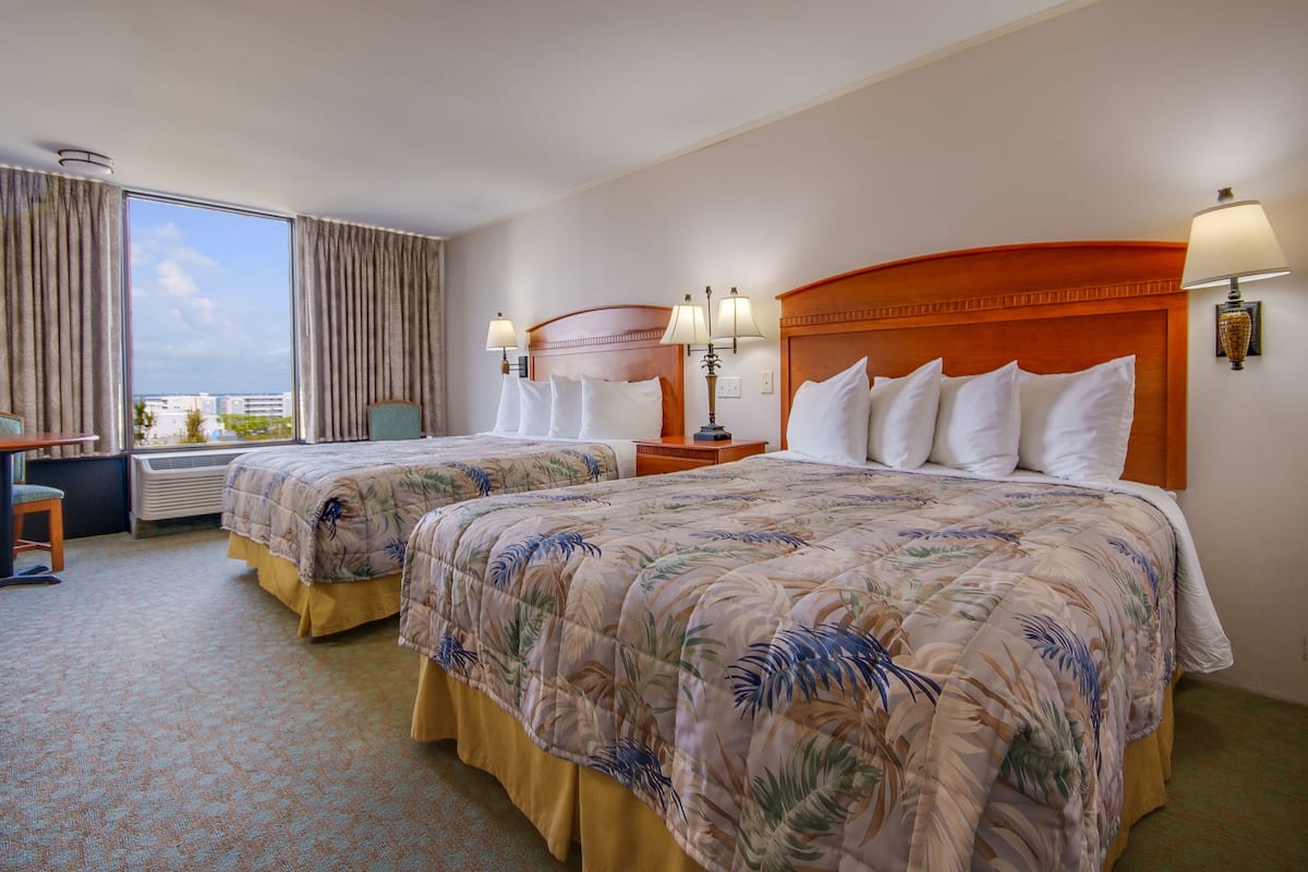 A hotel room with two beds, a desk, and a view of the city.