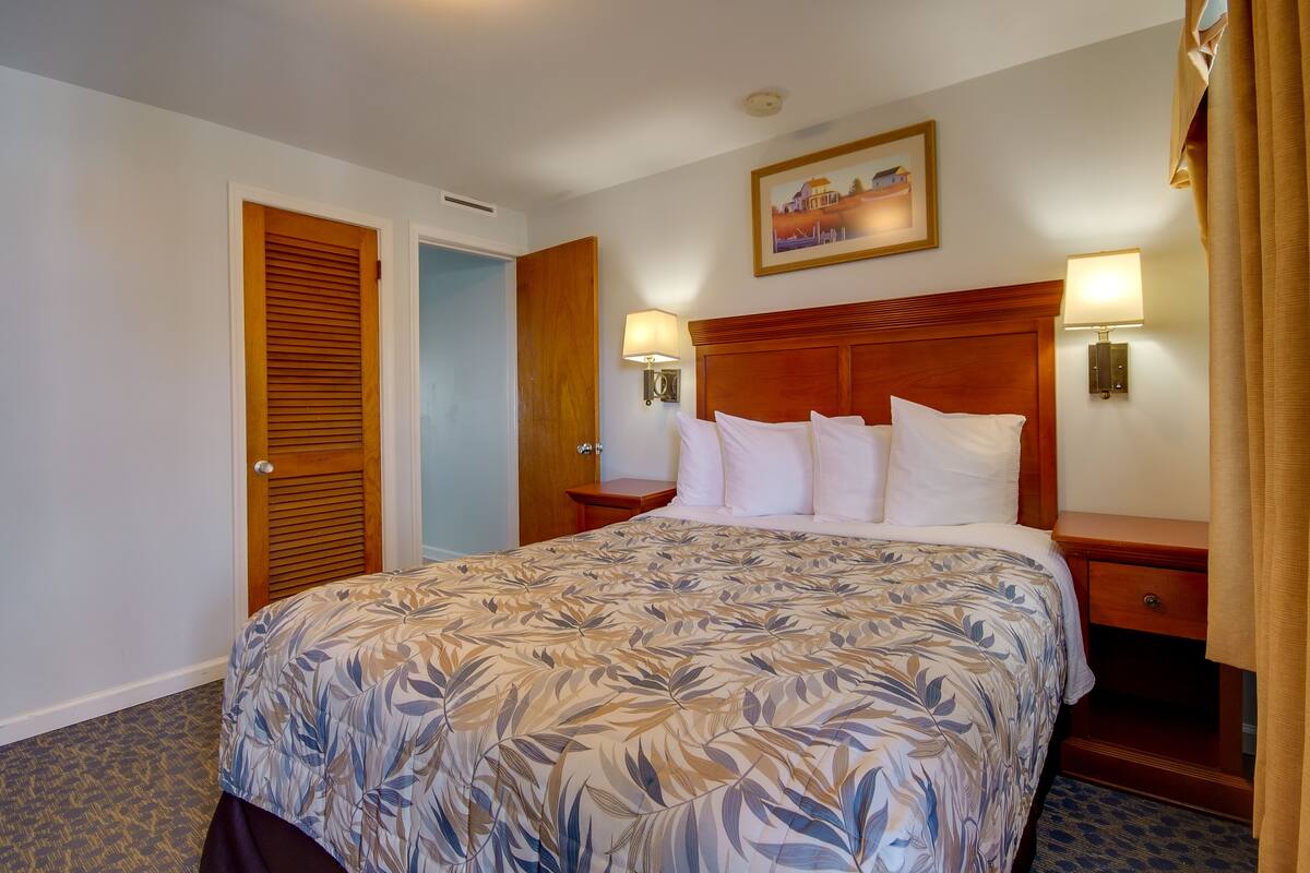 A hotel room with a large bed, two bedside tables with lamps, a wooden headboard, a door, and a framed picture on the wall.