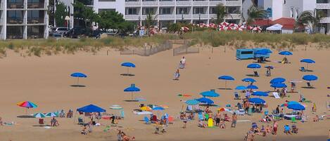 A beach with umbrellas and people. There are buildings in the background.