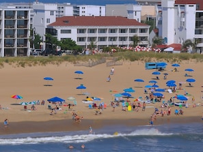A beach with umbrellas and people. There are buildings in the background.