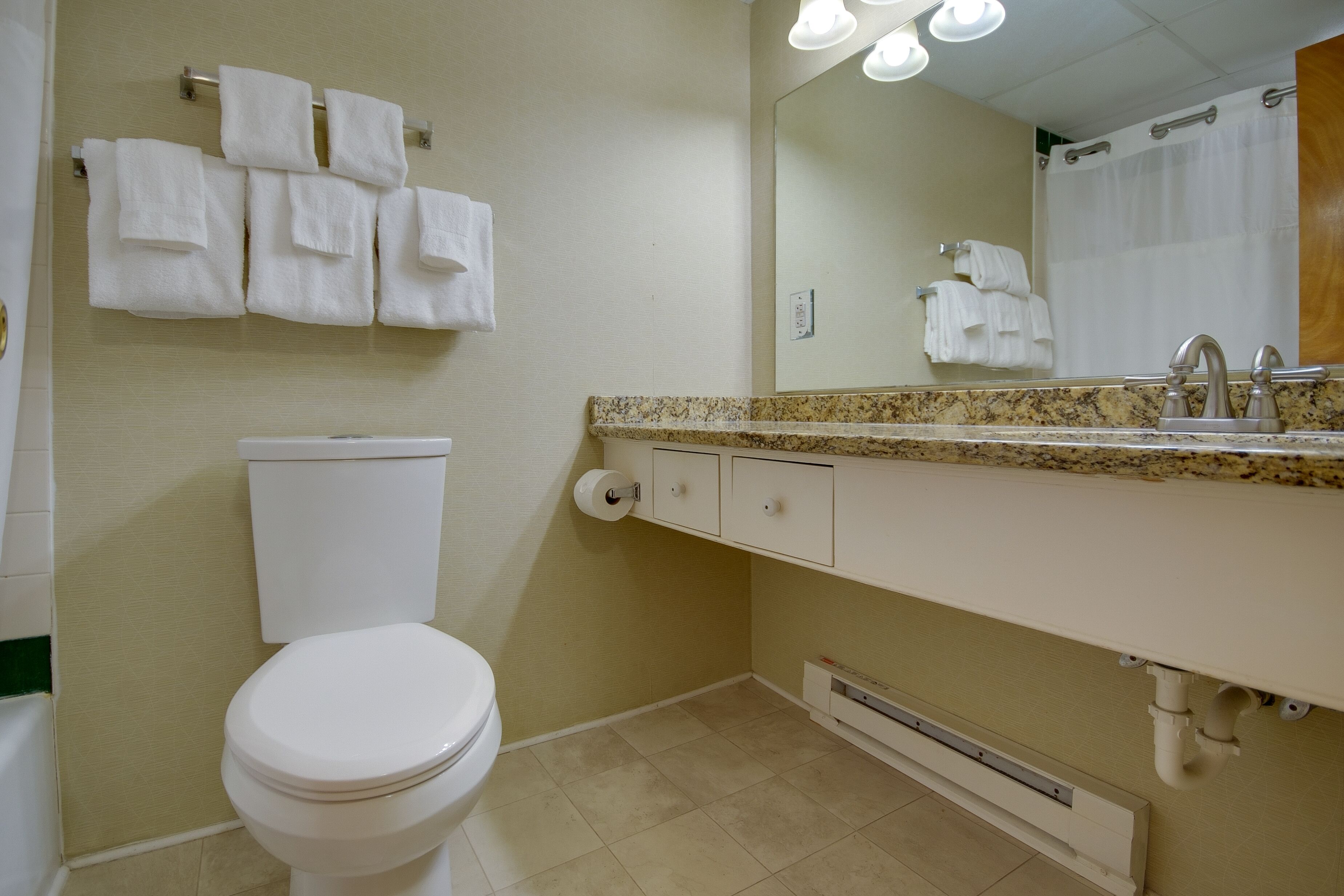 A bathroom with a toilet, a sink with a mirror, and a towel rack with multiple towels.
