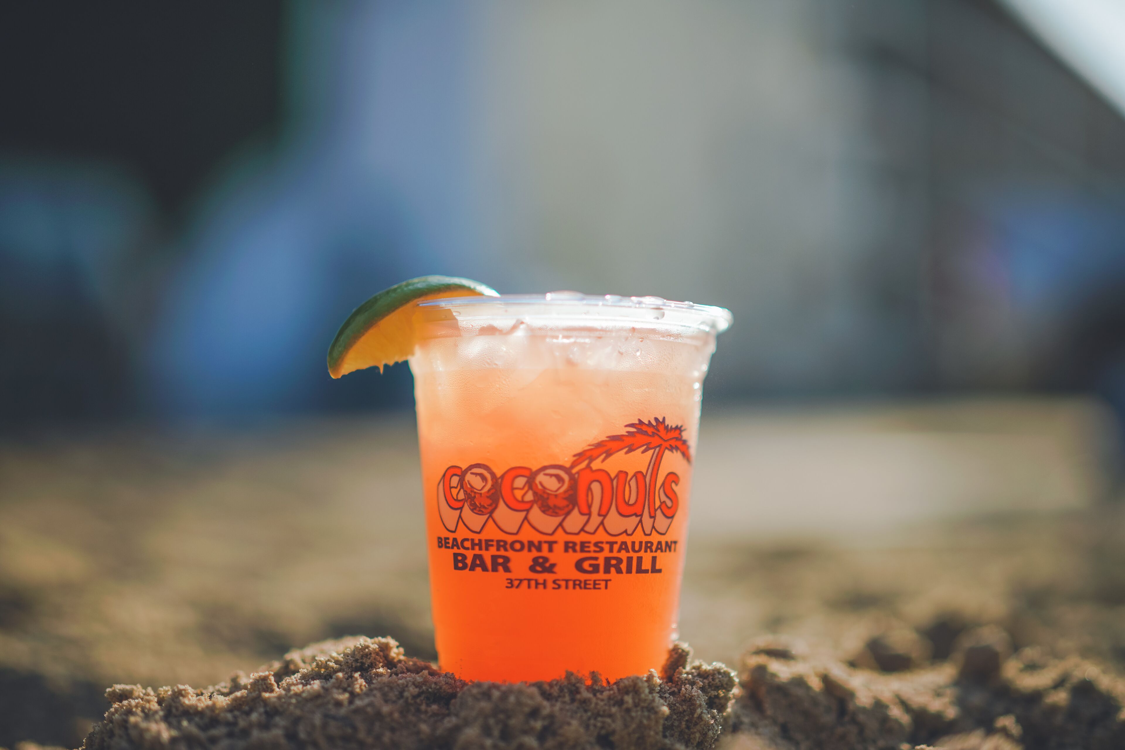 A drink in a plastic cup with a tropical design, placed on sand.
