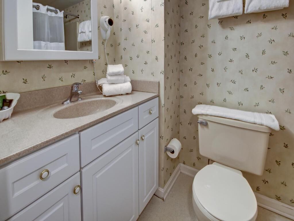 Une salle de bain équipée d’un lavabo, d’un miroir, de toilettes et d’un porte-serviettes.