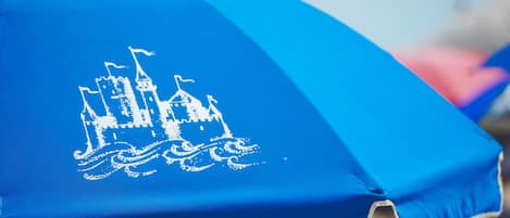 A blue umbrella with a white castle design and the text "The Sand Hotel".