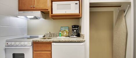 A compact kitchen with wooden cabinets, a microwave, a coffee maker, and a dishwasher.