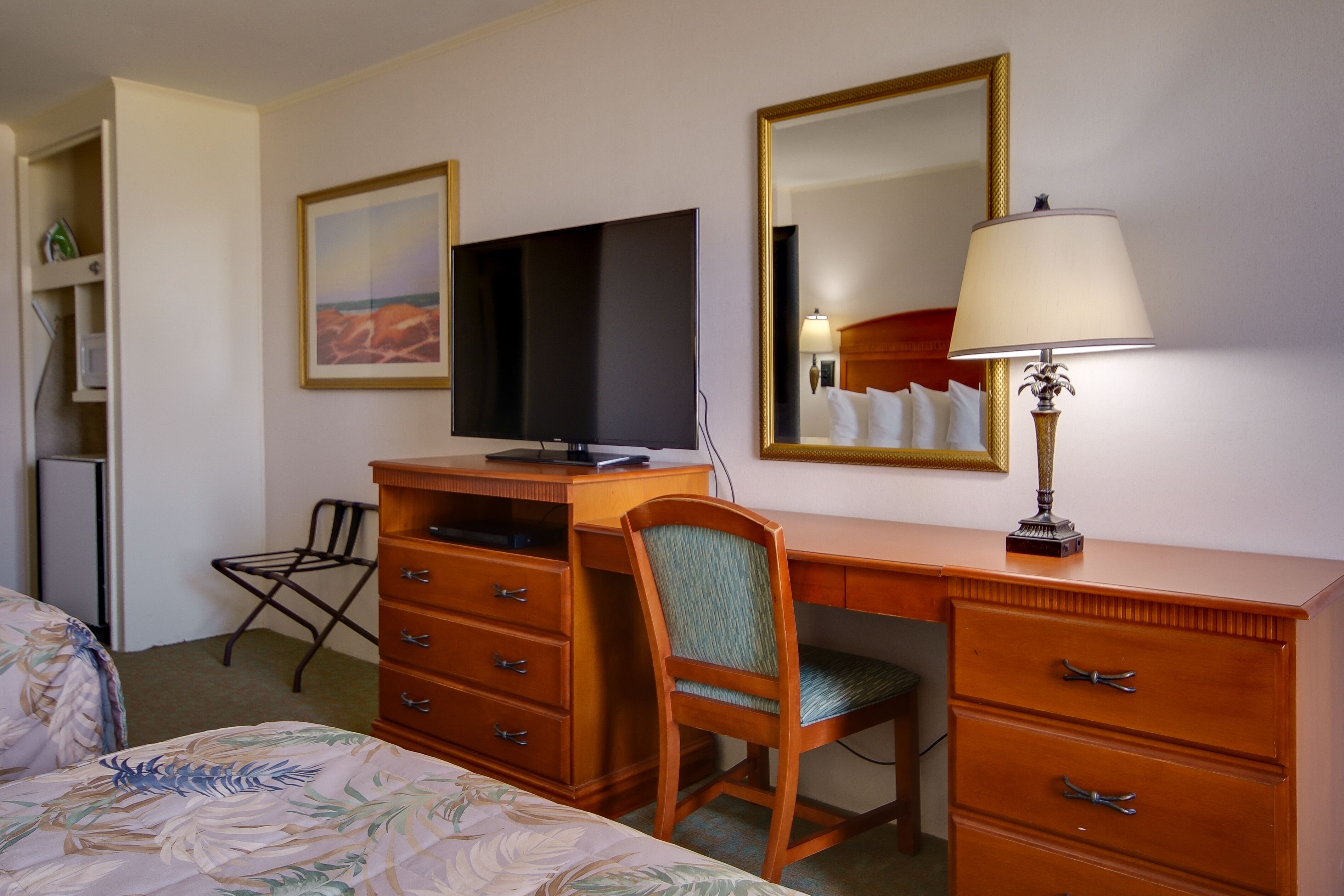 Une chambre d’hôtel comprenant un lit, un bureau avec une télévision, une chaise, une commode et une lampe.