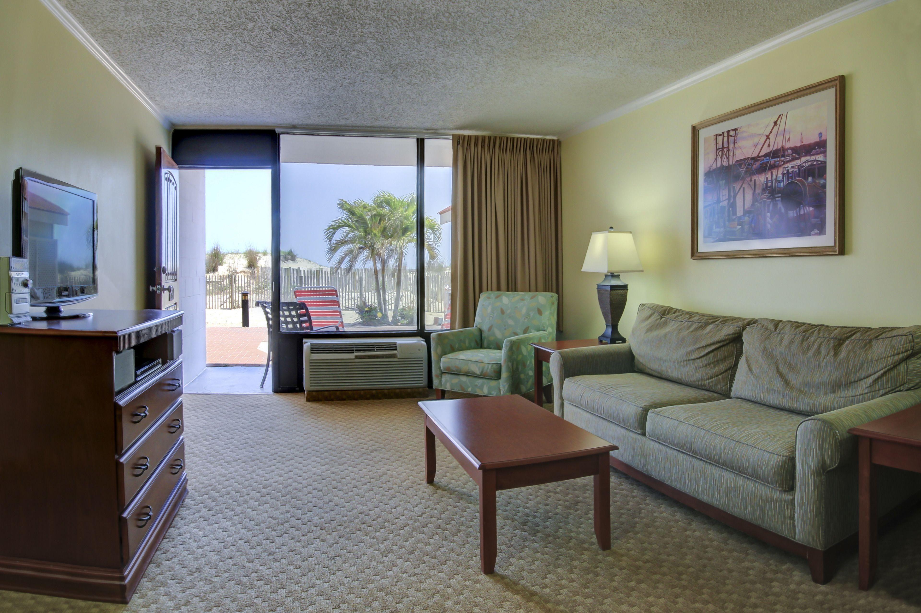 A hotel room with a large window, a sofa, a television, a desk, and a painting on the wall.