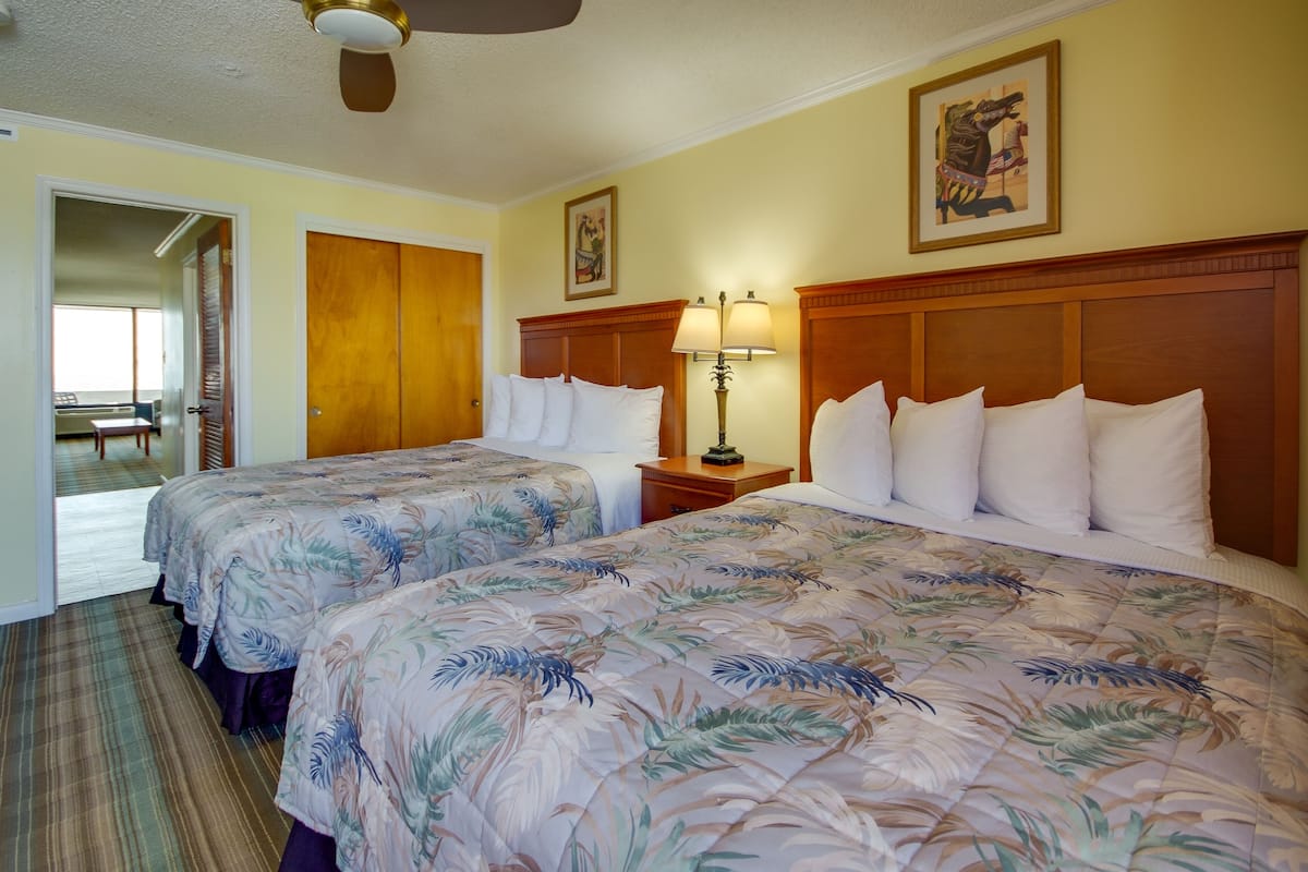 A hotel room with two beds, a wooden headboard, a nightstand with a lamp, and a painting on the wall.