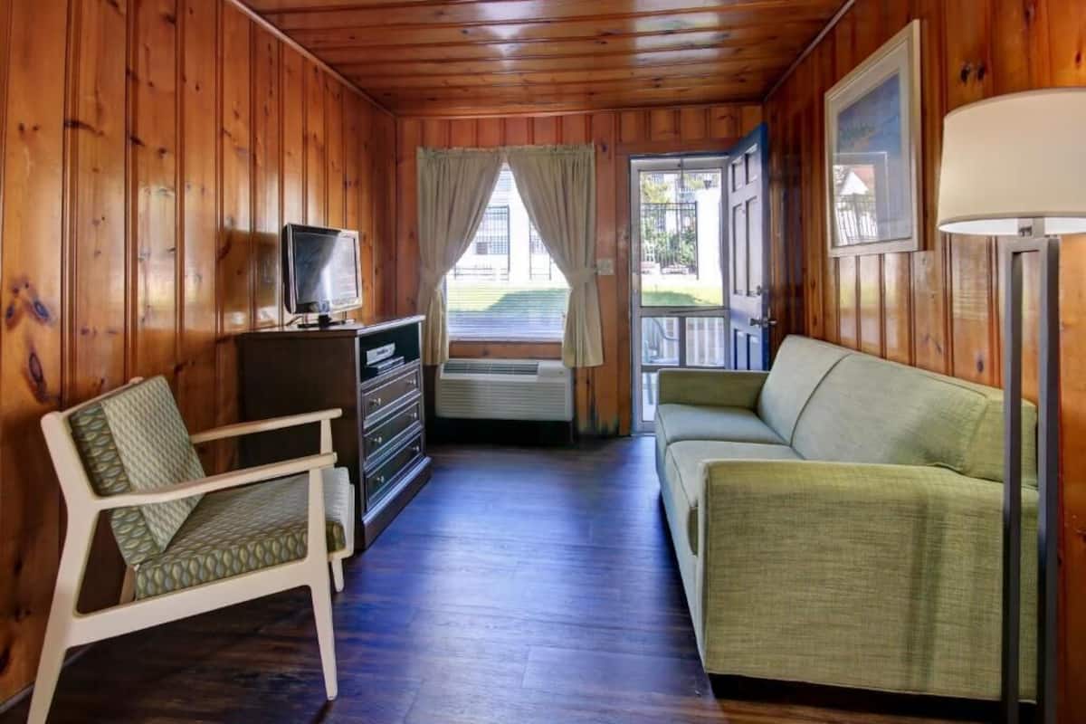 A wooden cabin interior with a sofa, a chair, a television, and a lamp.