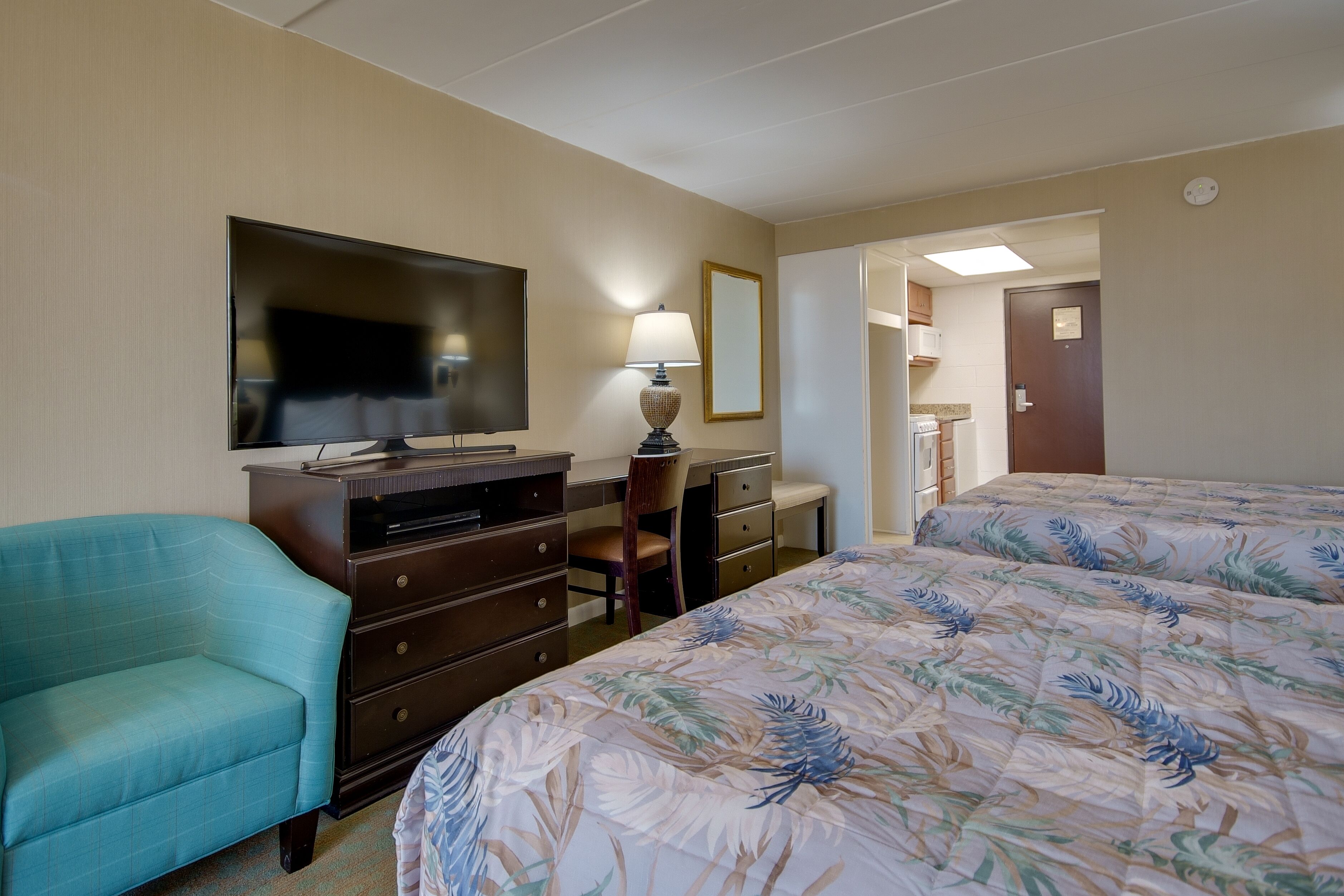 A hotel room with a bed, a desk, a chair, a television, and a dresser.