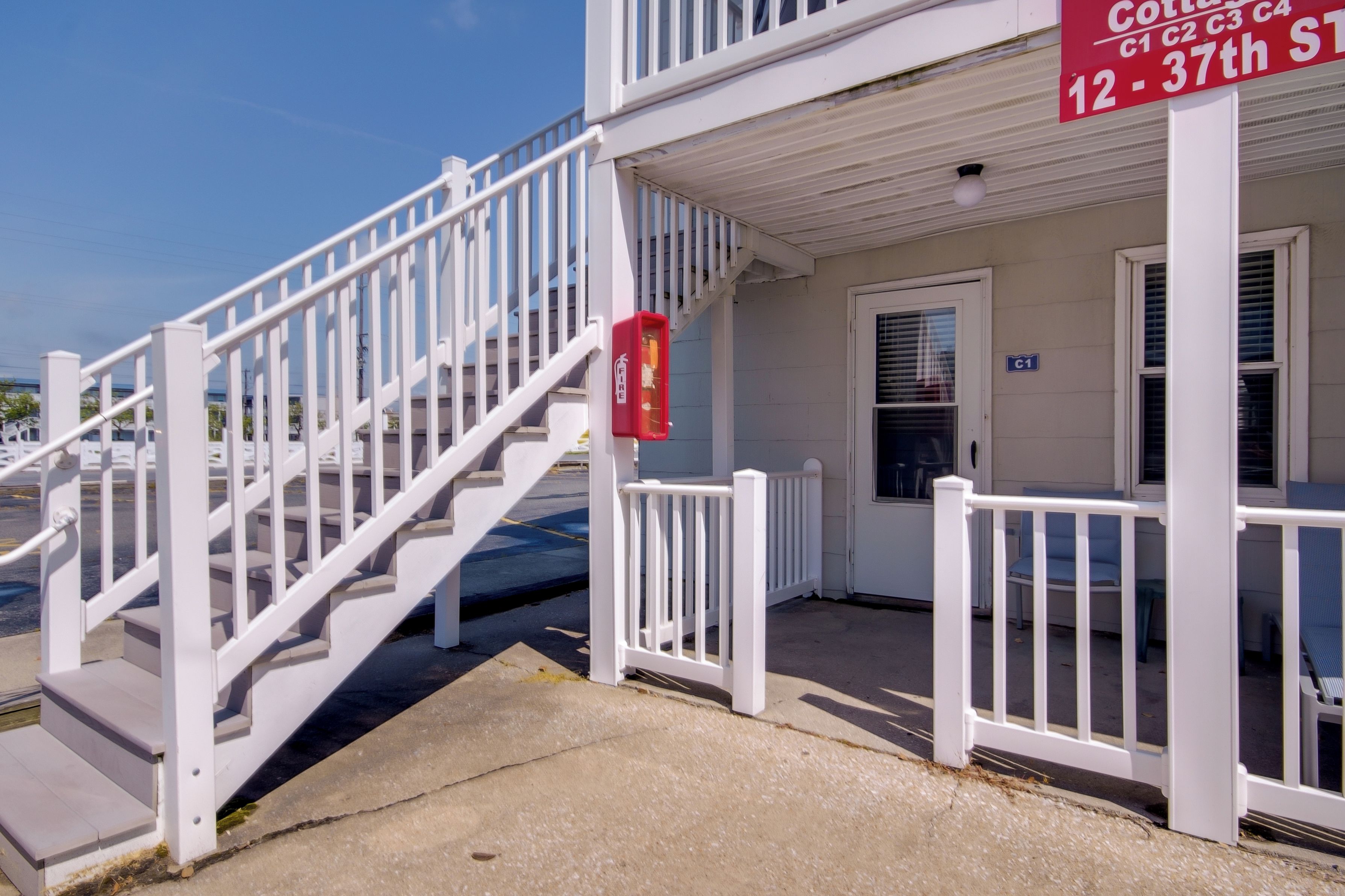 Un bâtiment blanc avec un escalier menant à une porte, un boîtier d’alarme incendie et une enseigne indiquant « Cottage C1 C2 C3 C4, 12-37, rue ».