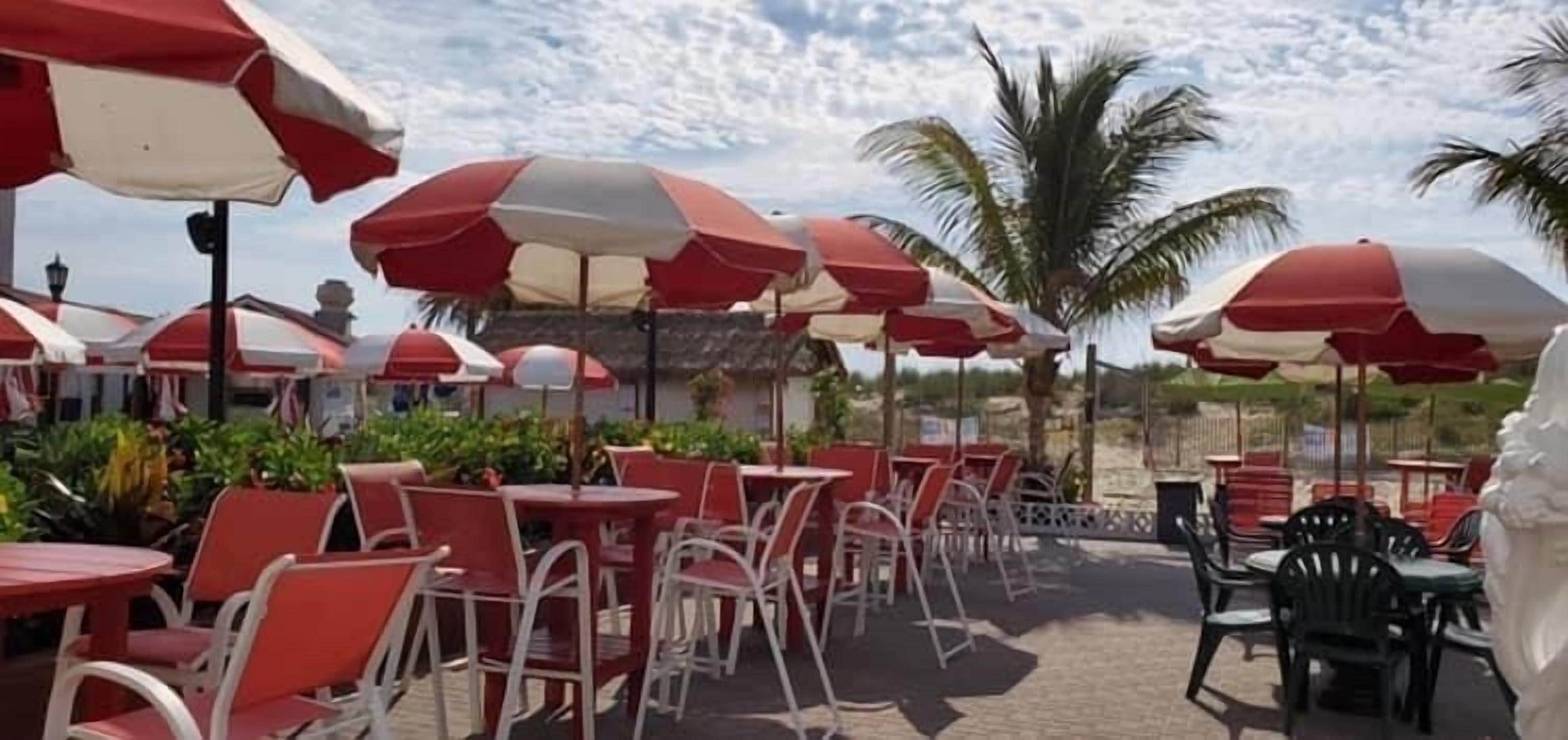 An outdoor seating area with red and white umbrellas, white chairs, and tables.