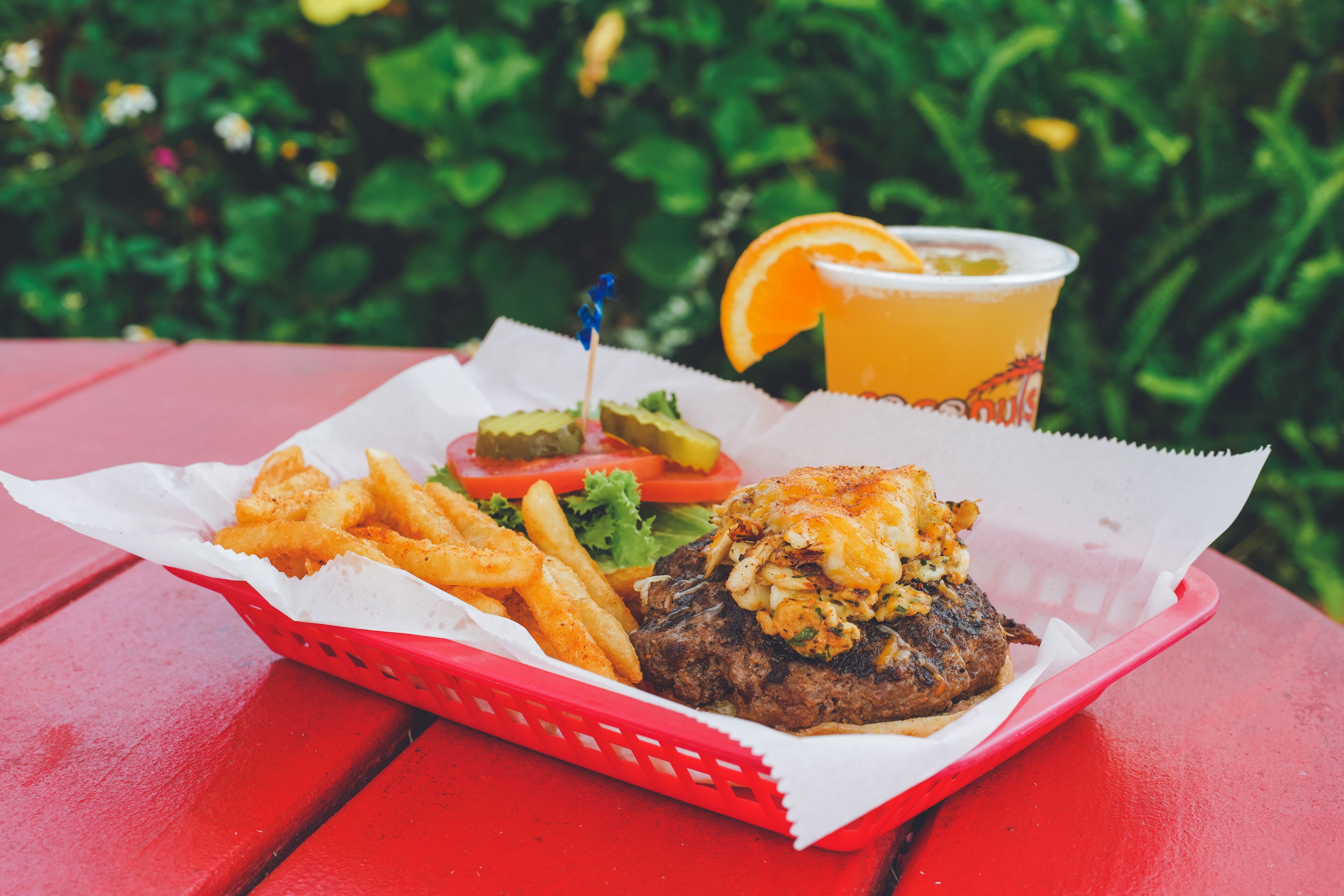 Comida con una hamburguesa, papas fritas y una bebida sobre una mesa roja.