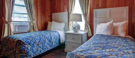A room with two beds, wooden walls, and a window with curtains.