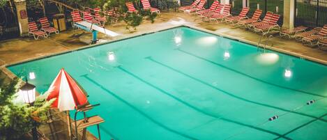 A swimming pool with red and white striped lounge chairs and umbrellas, surrounded by a fence and trees.