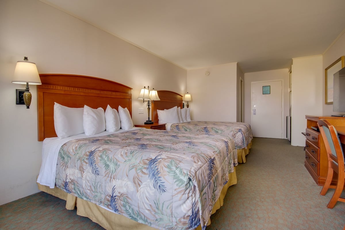 A hotel room with two beds, a dresser, and a desk.
