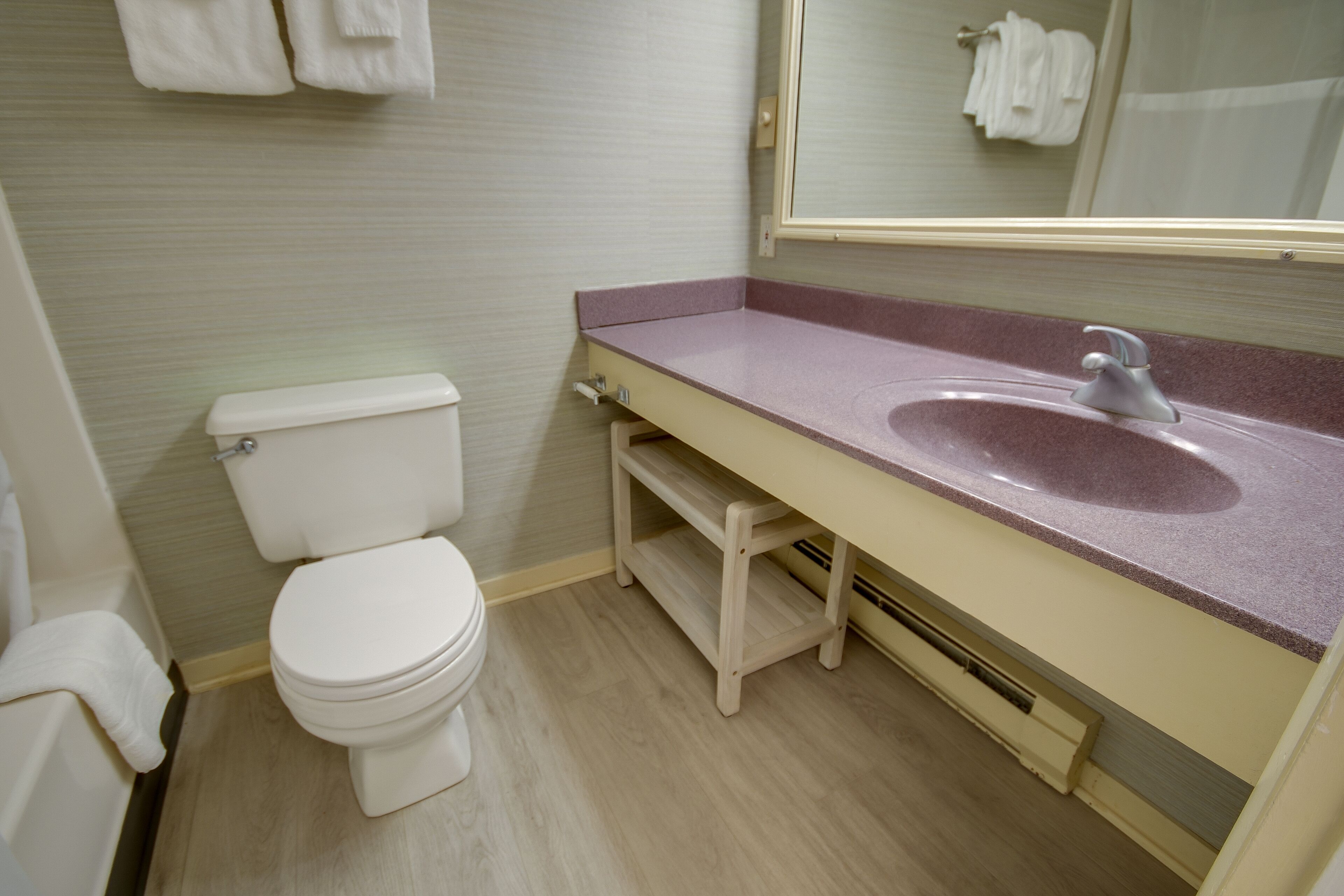 Ein Badezimmer mit einer weißen Toilette, einem beigen Waschtisch mit rosa Arbeitsplatte und einem Spiegel über dem Waschbecken.