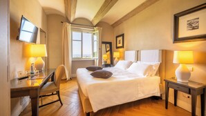 A hotel room with a bed, bedside tables with lamps, a desk with a chair, and a window with curtains. - Relais Villa D'Amelia (Benevello)