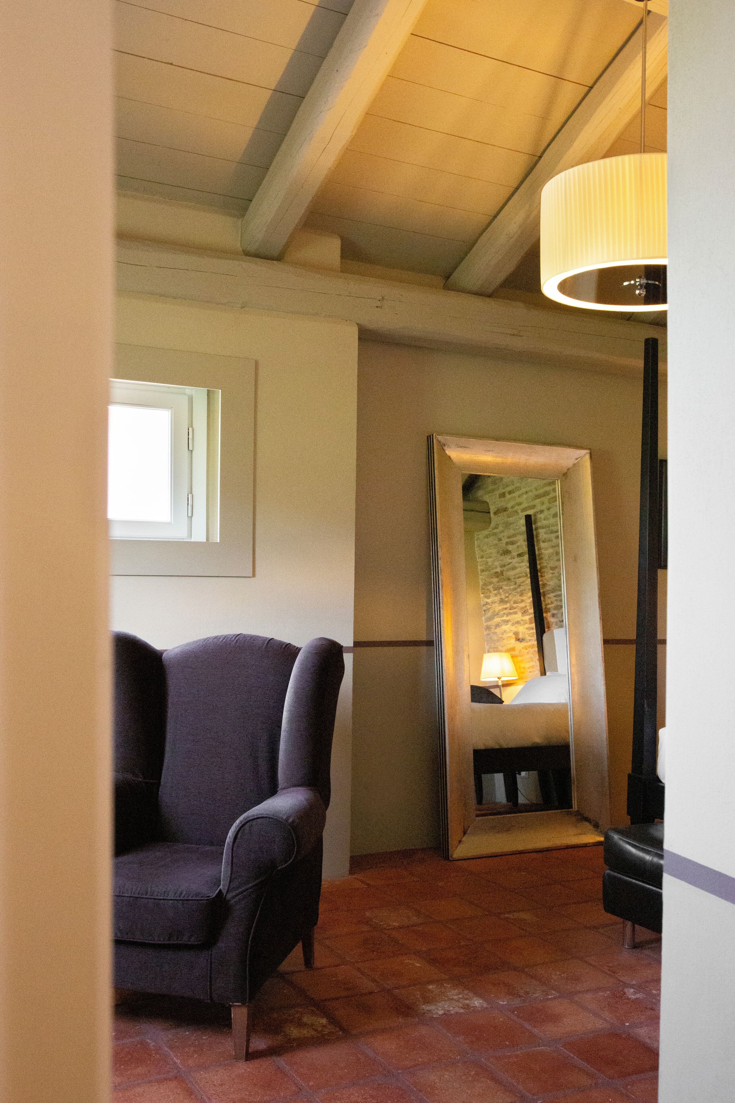 Ein Zimmer mit einem Sessel, einem Spiegel, einer Lampe und einem Fenster.