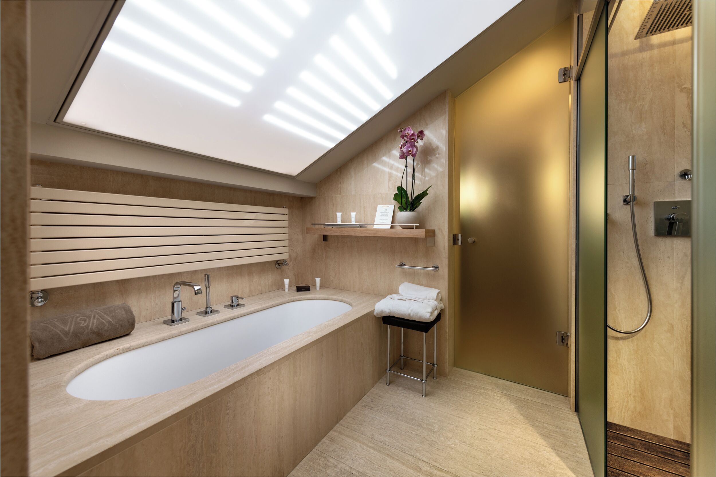 Ein modernes Badezimmer mit einer großen Badewanne, einem kleinen Waschbecken, einem Handtuchhalter und einer Duschkabine.