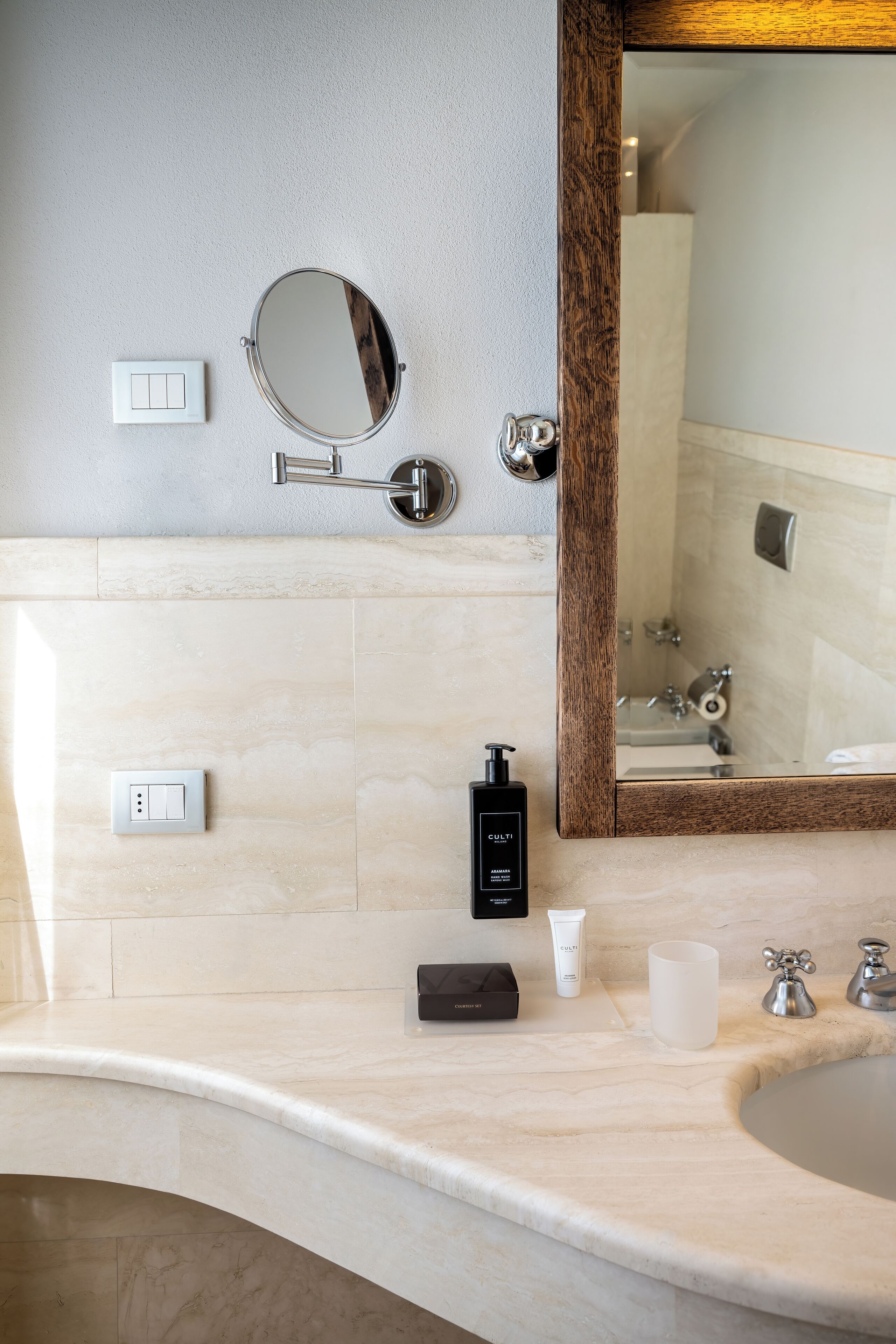 A bathroom with a marble countertop, a round mirror, a wooden-framed mirror, a sink, and toiletries.
