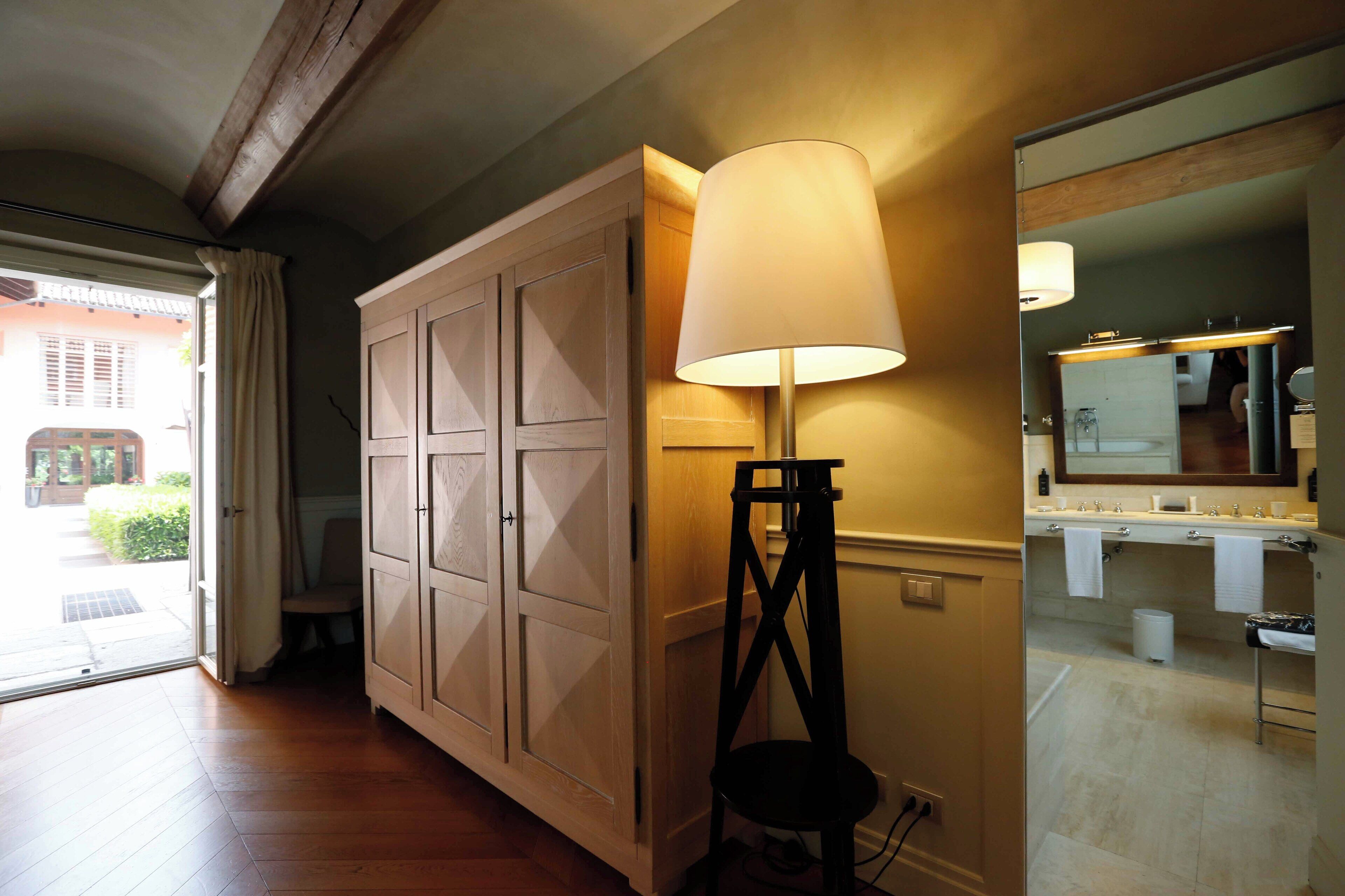 A hallway with wooden flooring, a large cabinet, a standing lamp, and a bathroom visible through an open door.