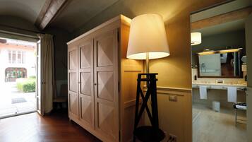 A hallway with wooden flooring, a large cabinet, a standing lamp, and a bathroom visible through an open door.