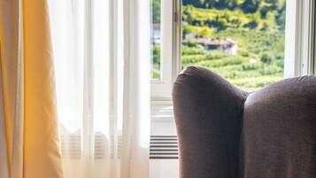 Une pièce avec vue sur un paysage verdoyant, visible à travers une fenêtre, comprenant une chaise et un rideau.
