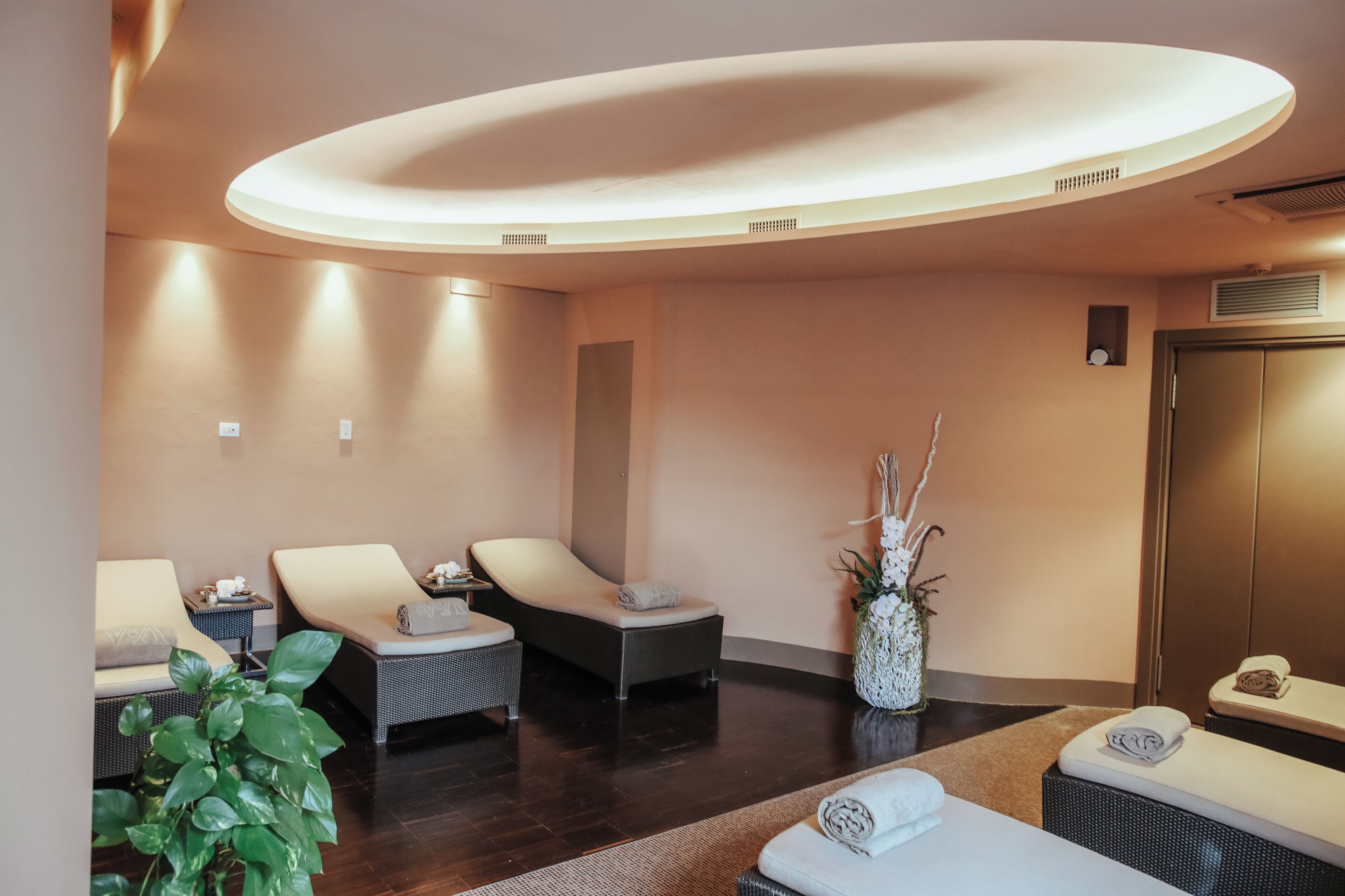 Un cuarto de spa con dos sillones de masaje, una mesita con una toalla, una planta en maceta y un mostrador de recepción.