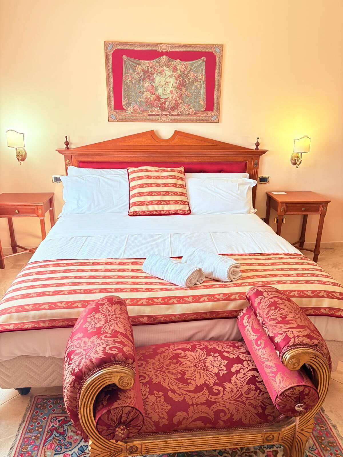 A hotel room with a large bed, two bedside tables, a headboard, and a decorative wall hanging.