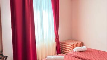 A hotel room with two beds, red bedding, a white towel, and a window with red curtains.