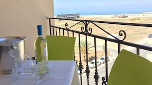 A balcony with a table set for two, a bottle of wine, and a pot. The view includes a beach and a building in the distance. - Hotel D'Angelo Palace (Mazara del Vallo)