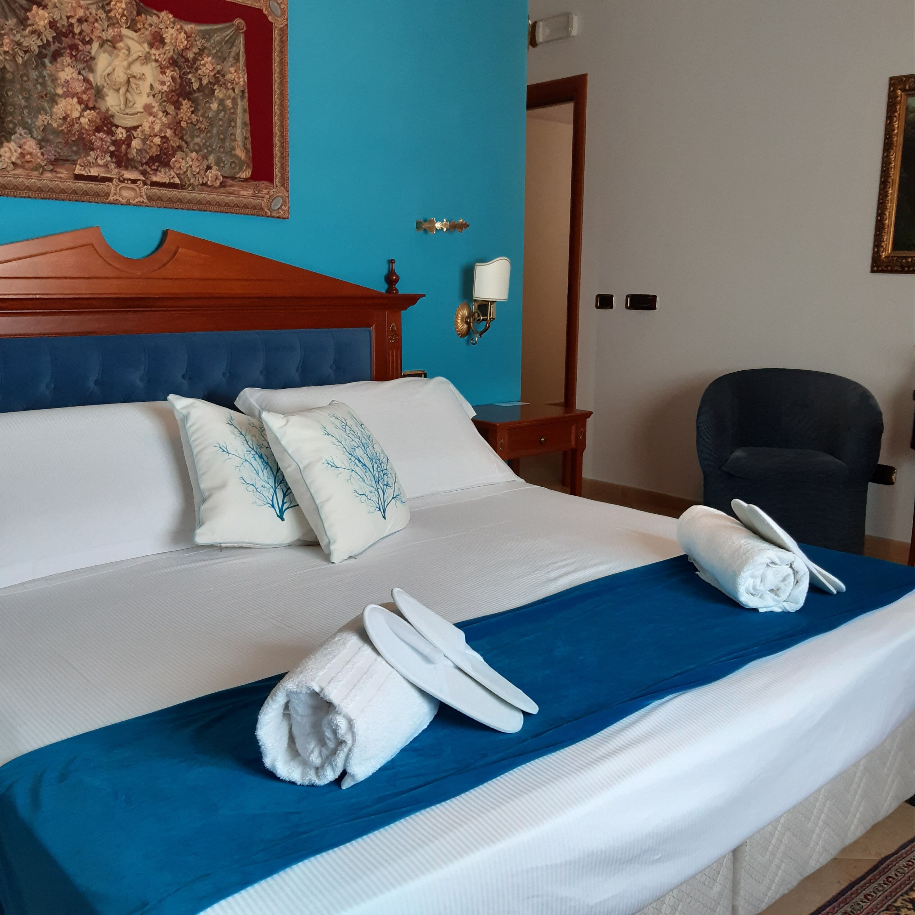 A neatly made bed with white linens and blue accents, a wooden headboard, and a painting on the wall.