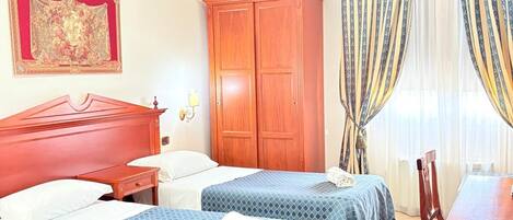 A hotel room with three beds, a wooden wardrobe, a desk, and a chair.