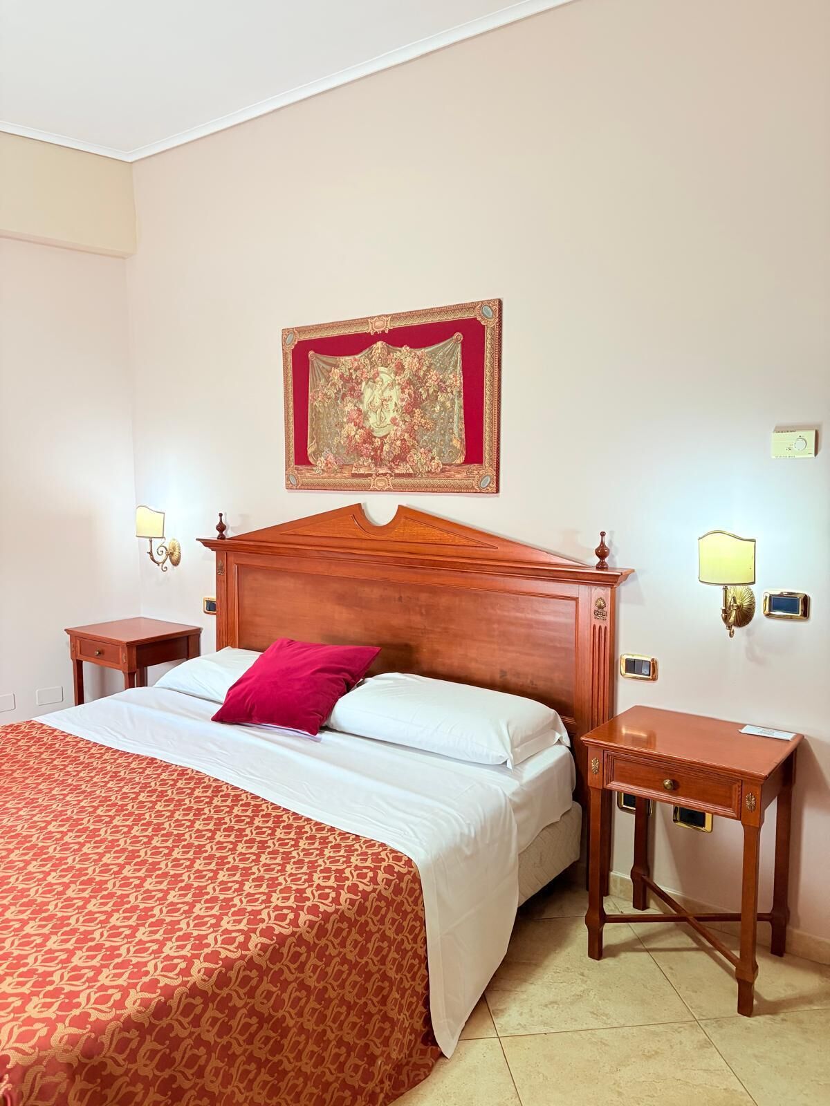 Une chambre d’hôtel avec un grand lit, une tête de lit en bois, deux tables de chevet et un miroir décoratif au mur.