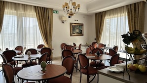 A hotel dining area with multiple round tables and chairs, a chandelier, and a painting on the wall. - Hotel D'Angelo Palace (Mazara del Vallo)