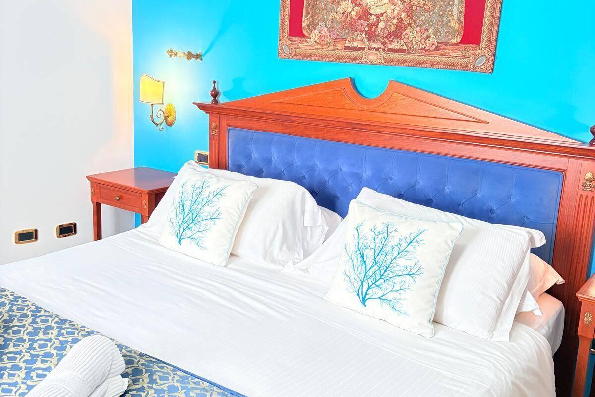 Een netjes opgemaakt bed met wit- en blauwe beddengoed, een blauw hoofdbord en een decoratieve wandhanger.