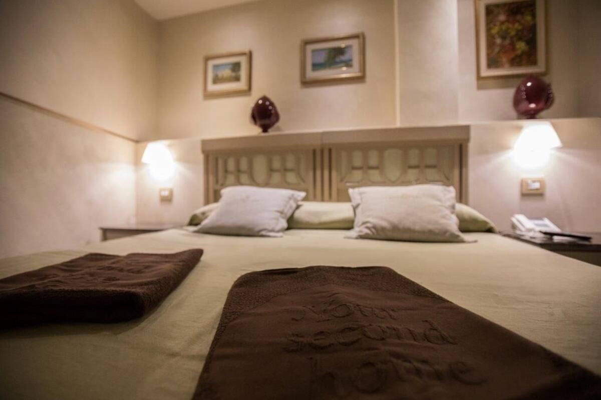 A hotel room with a bed, two bedside lamps, and a nightstand with a phone.