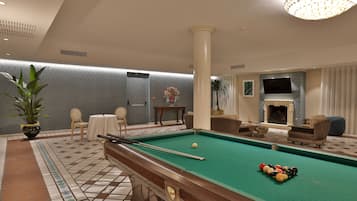 Ein Billardtisch mit Kugeln, eine Lounge mit Sesseln, ein Kamin und ein Fernseher.