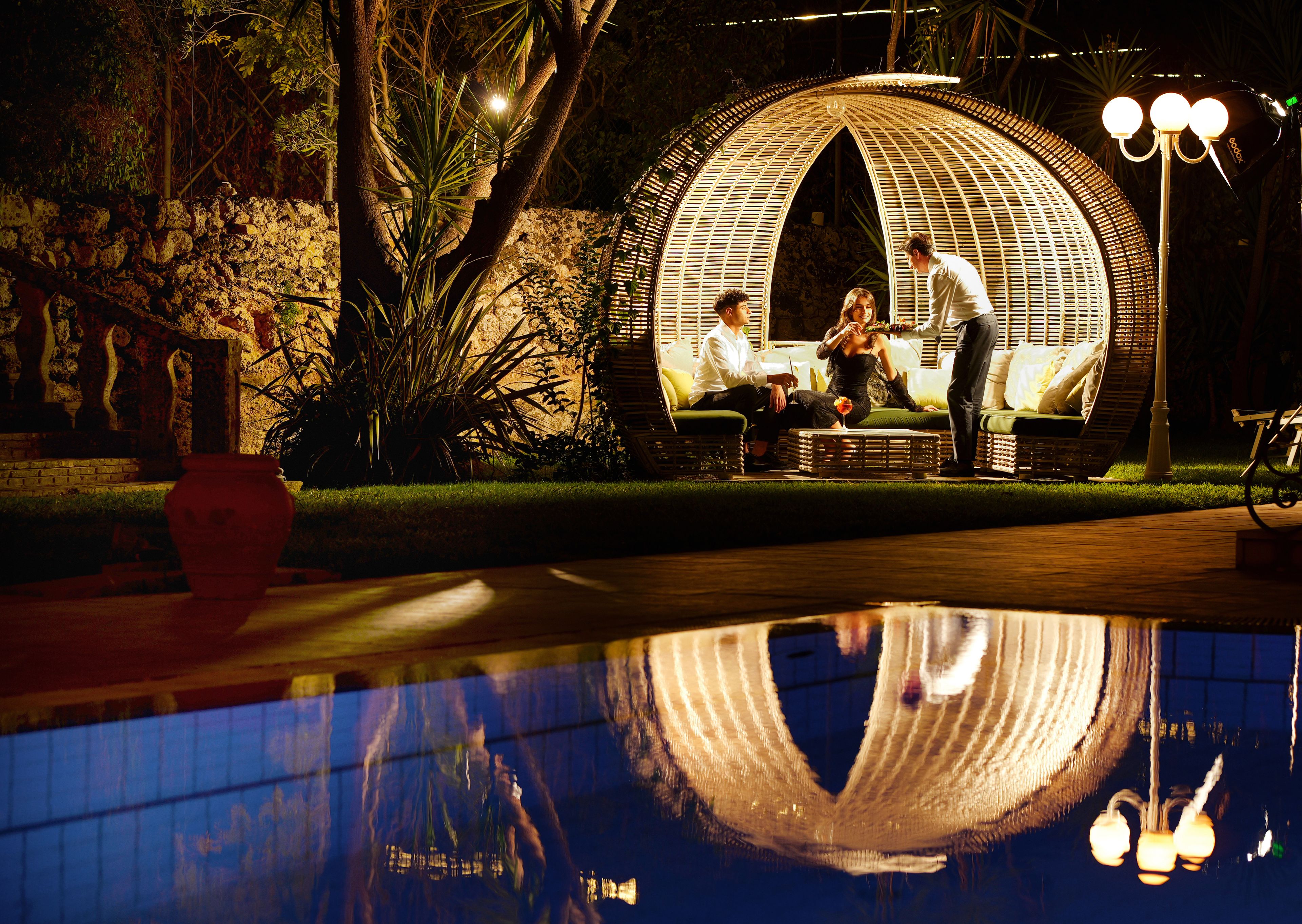 Un espace extérieur aménagé avec des sièges, une structure sphérique originale, un bassin d’eau réfléchissant et un lampadaire.