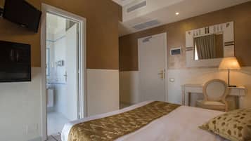 Habitación de hotel con cama, escritorio, silla, televisión y baño visible a través de una puerta abierta.