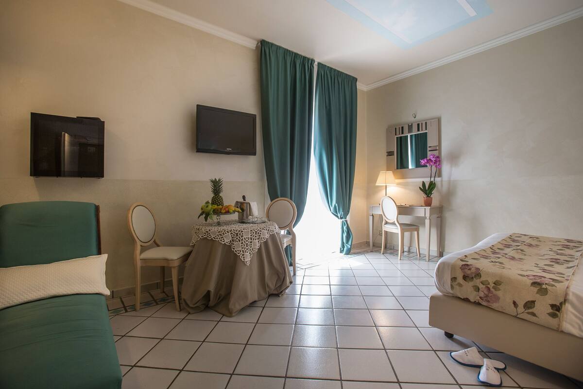 A hotel room with a bed, a desk, a chair, a TV, and a window with curtains.