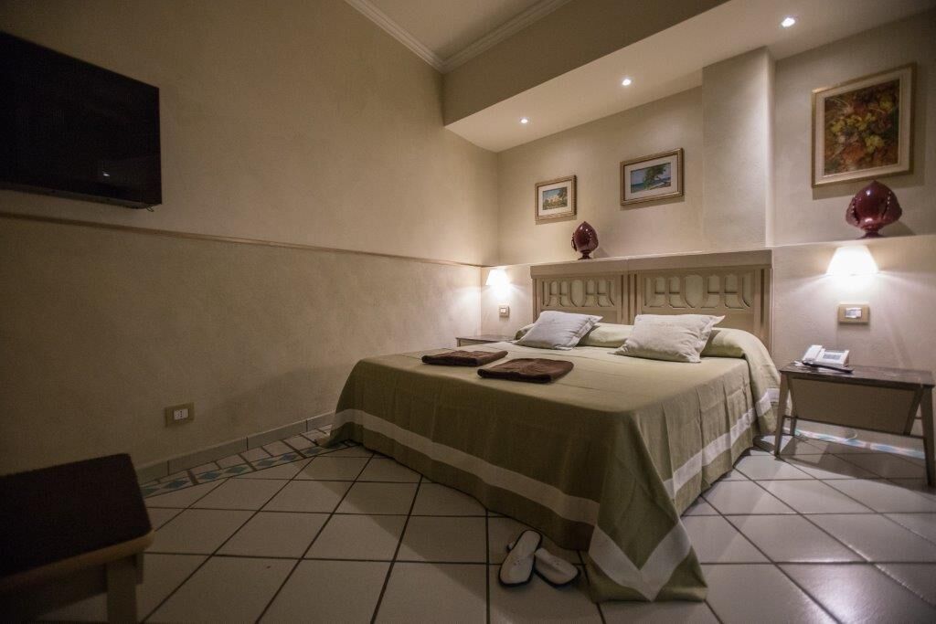 A hotel room with a bed, a nightstand, a chair, and a television on the wall.
