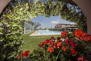 A swimming pool surrounded by red flowers and greenery, with a building in the background. - Mancini Park Hotel (Rome)