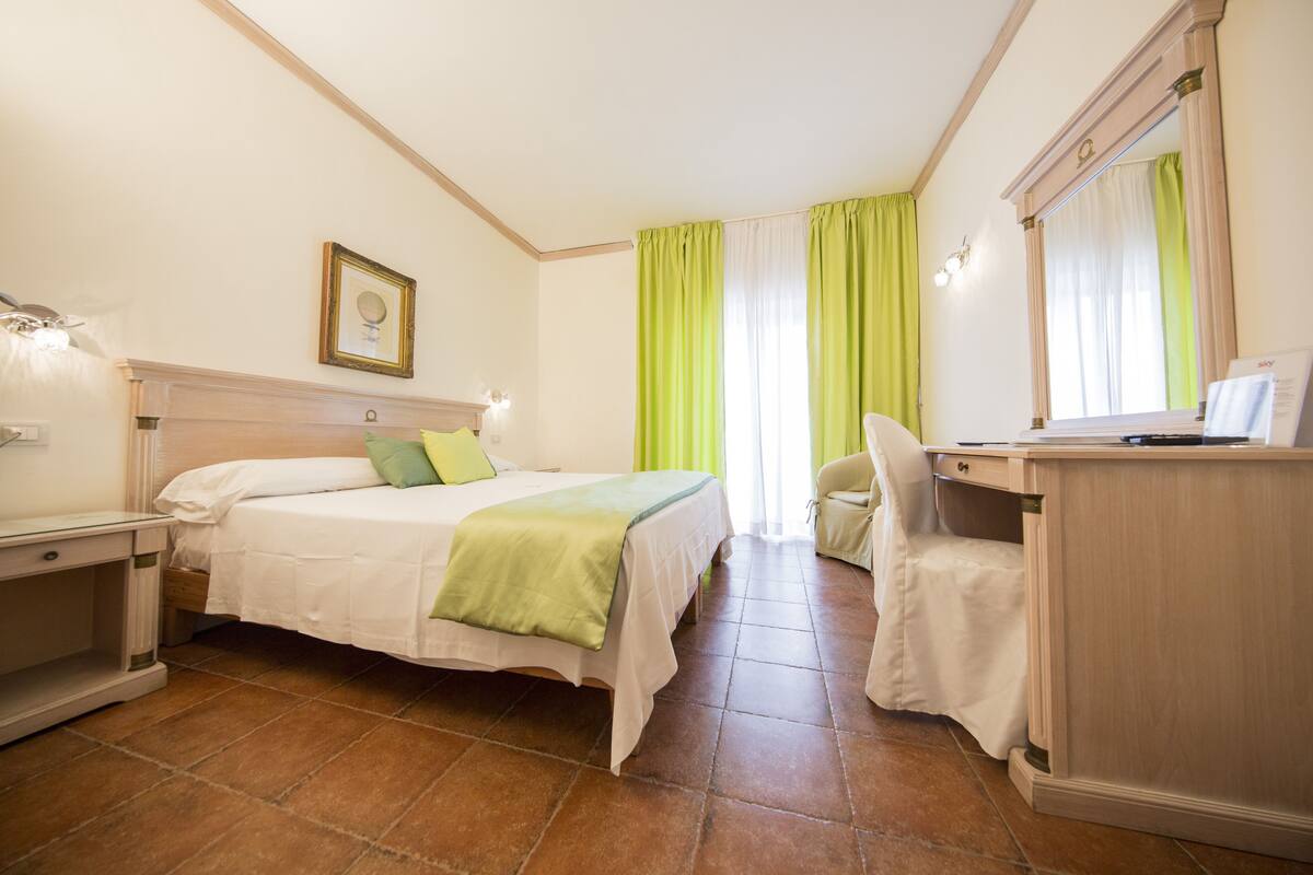 A hotel room with a bed, a desk, a chair, and a mirror.