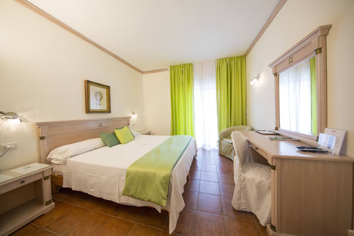 A hotel room with a bed, desk, chair, and a large mirror.