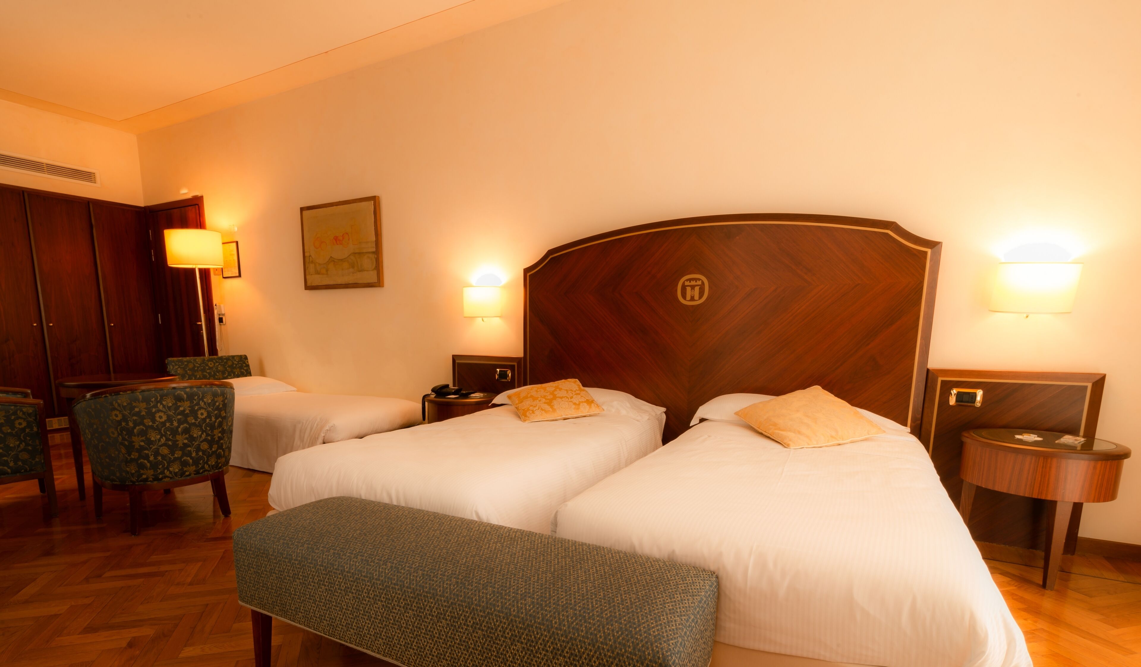 Habitación de hotel con dos camas, un banco, un escritorio y una silla.